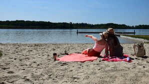 Ein Strand mit einer roten Decke, einem Thermosbehälter und einer Tasche im Sand.