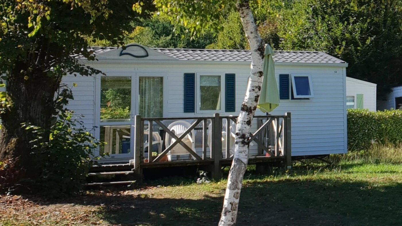 A mobile home with a deck, surrounded by trees and greenery.
