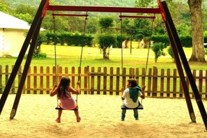 Eine Schaukel im Park, mit Holzzaun und Grün im Hintergrund.