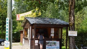 Pieni puinen rakennelma, jossa on kyltti, henkilö seisomassa sisäänkäynnin luona ja pyörä, joka on pysäköity lähelle.