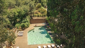 Une piscine extérieure dotée d’une terrasse en bois, entourée d’une végétation luxuriante et d’arbres.