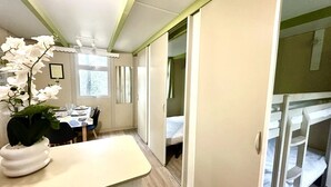 Une chambre d’hôtel compacte avec un lit superposé, un petit coin repas avec une table et des chaises, et une plante en pot.