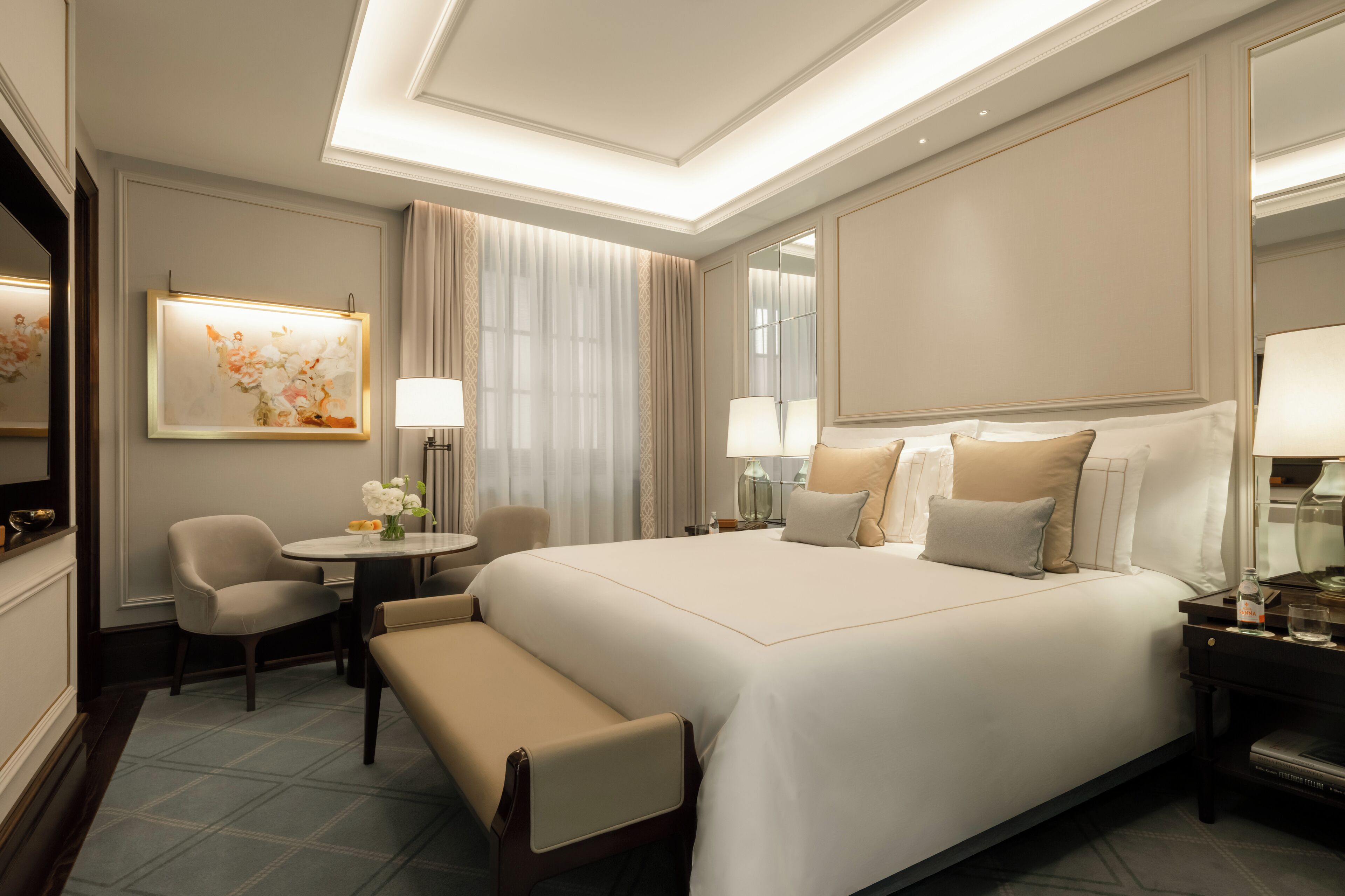 Una habitación de hotel con una cama grande, un área de descanso con una mesa y sillas, y un espejo en la pared.