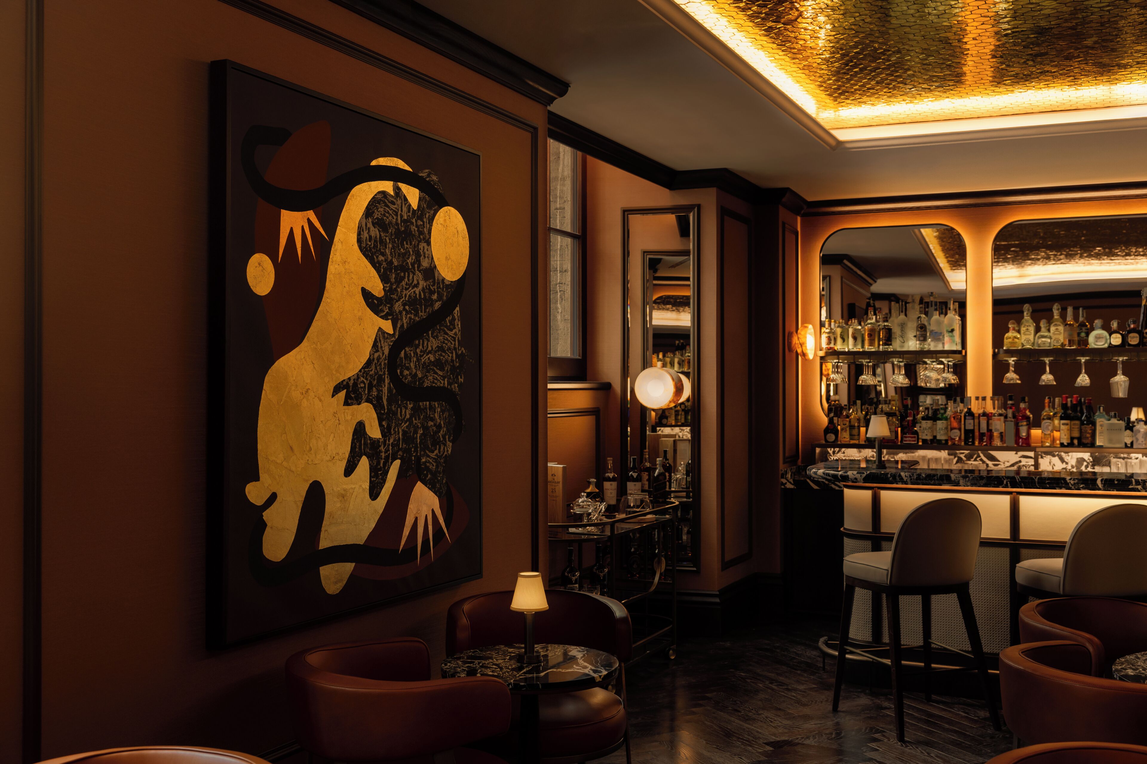 Un espace bar agrémenté d’un grand tableau abstrait, de fauteuils en cuir et d’un bar bien garni.