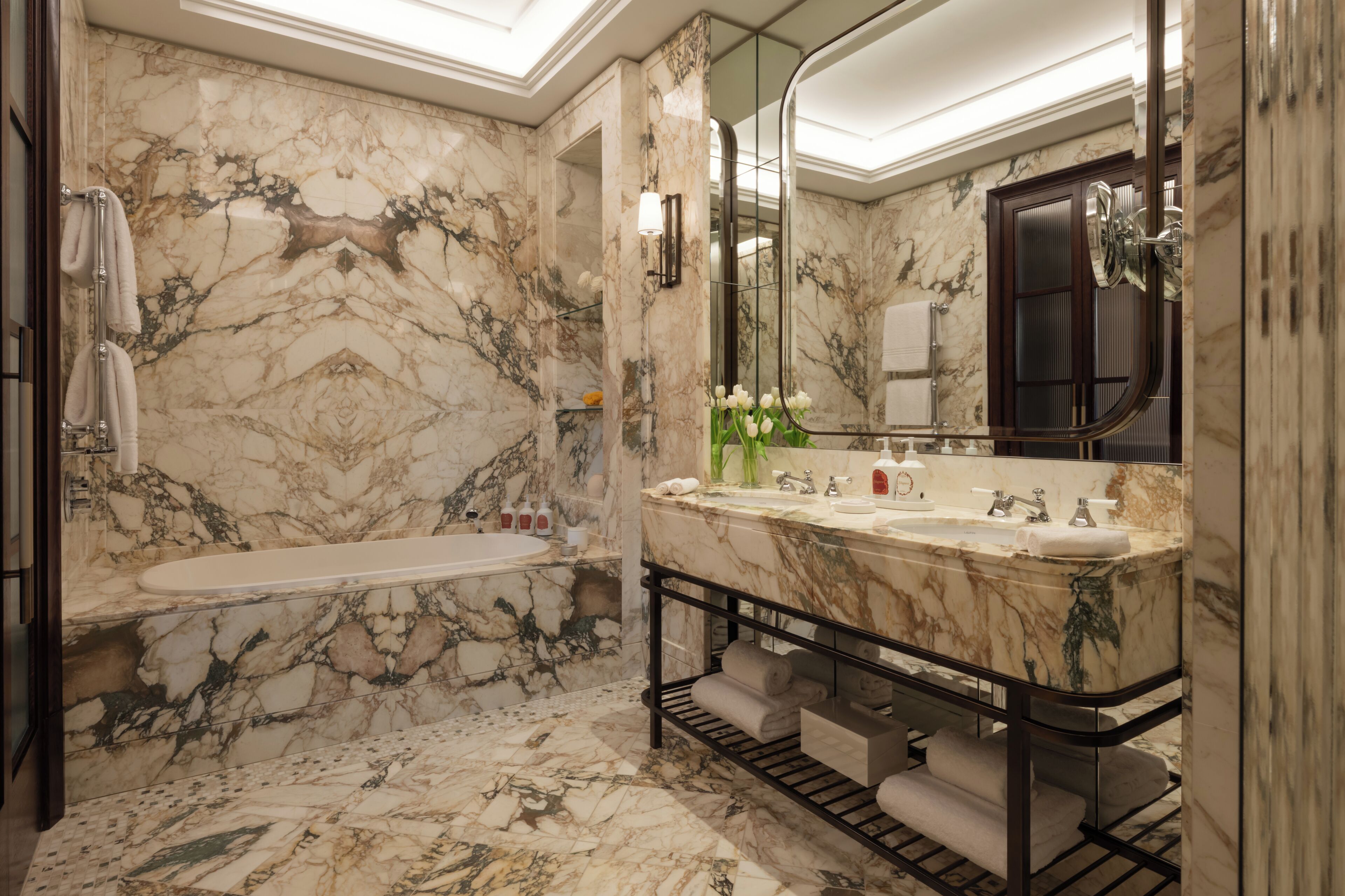 A marble bathroom with a bathtub, two sinks, a vanity, and a large mirror.