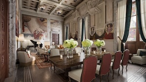 A grand room with a large wooden table, red upholstered chairs, and a piano. - Corinthia Rome (Rome)