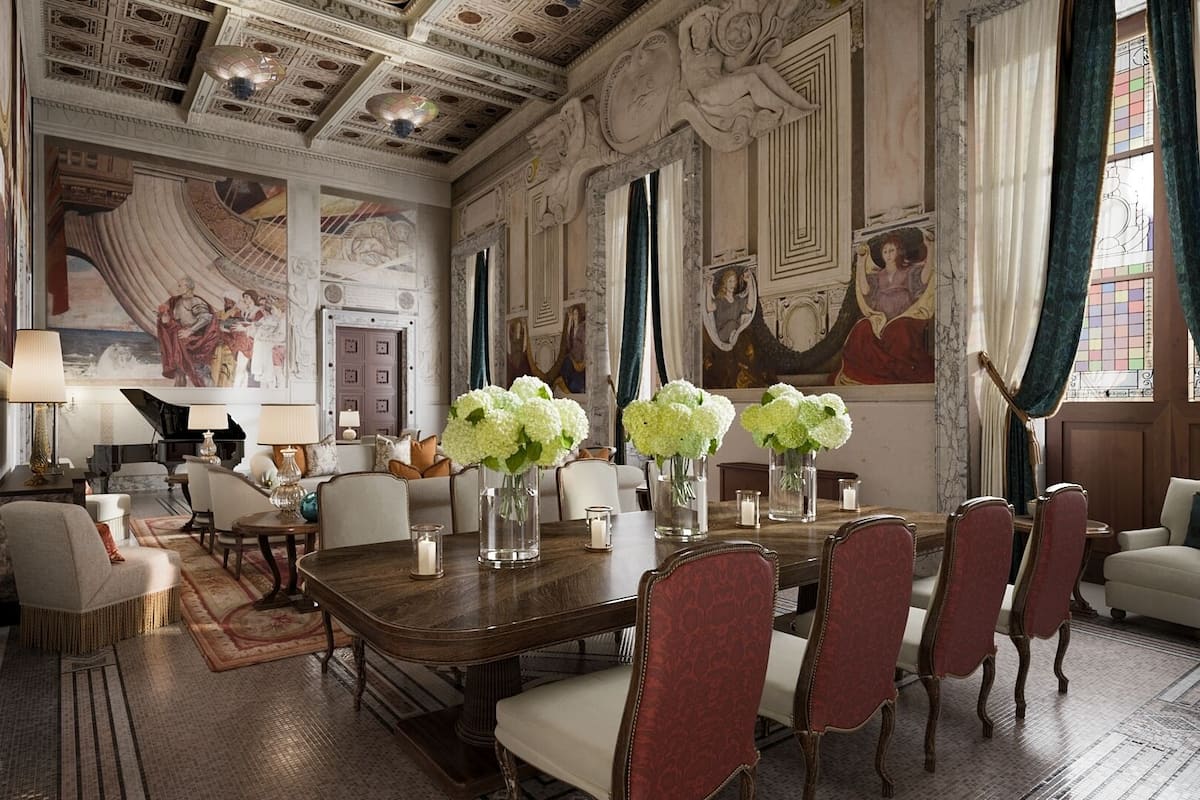 A grand room with a large wooden table, red upholstered chairs, and a piano.