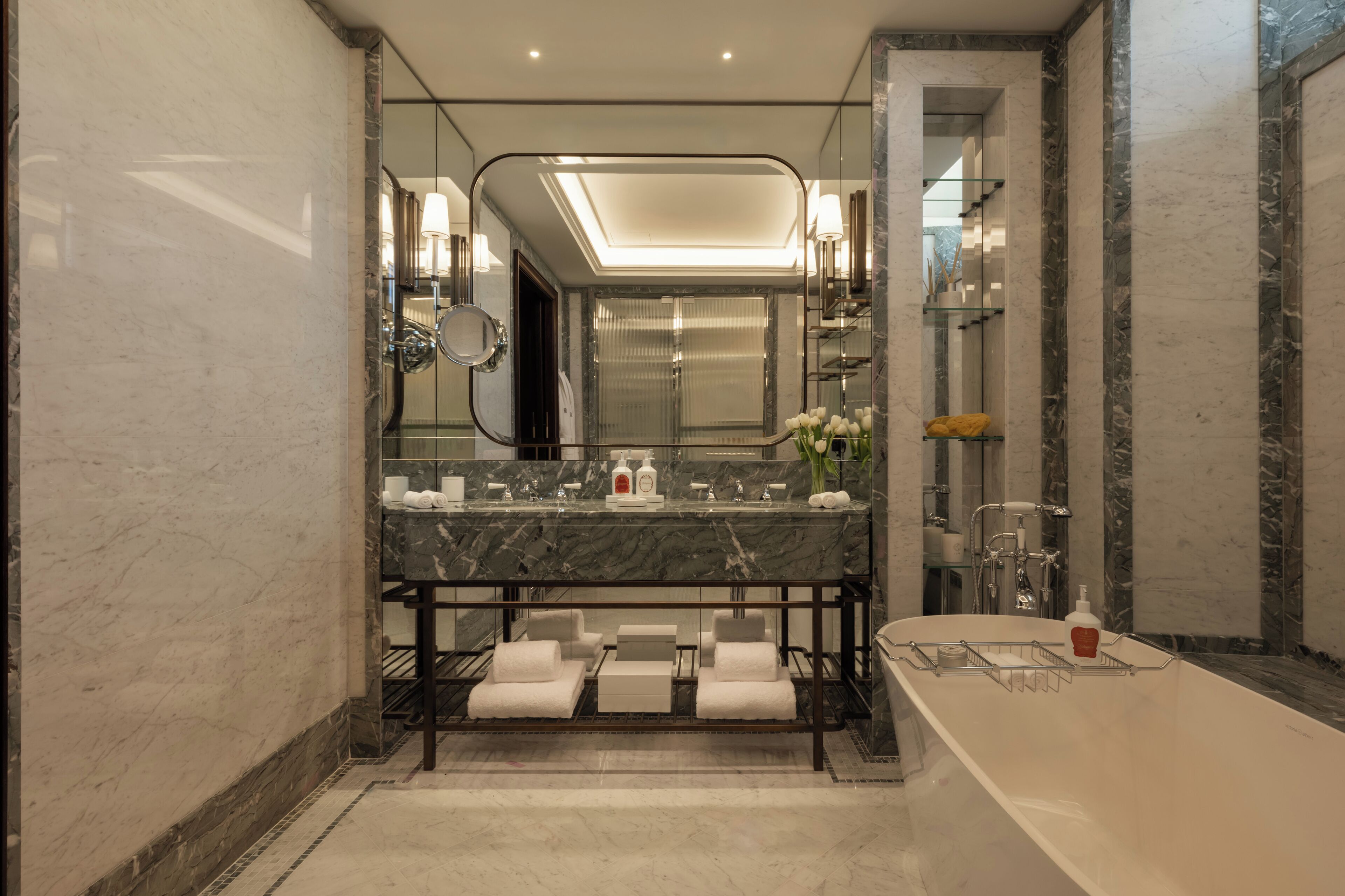A modern bathroom with a marble vanity, a large mirror, a bathtub, and a glass shower enclosure.