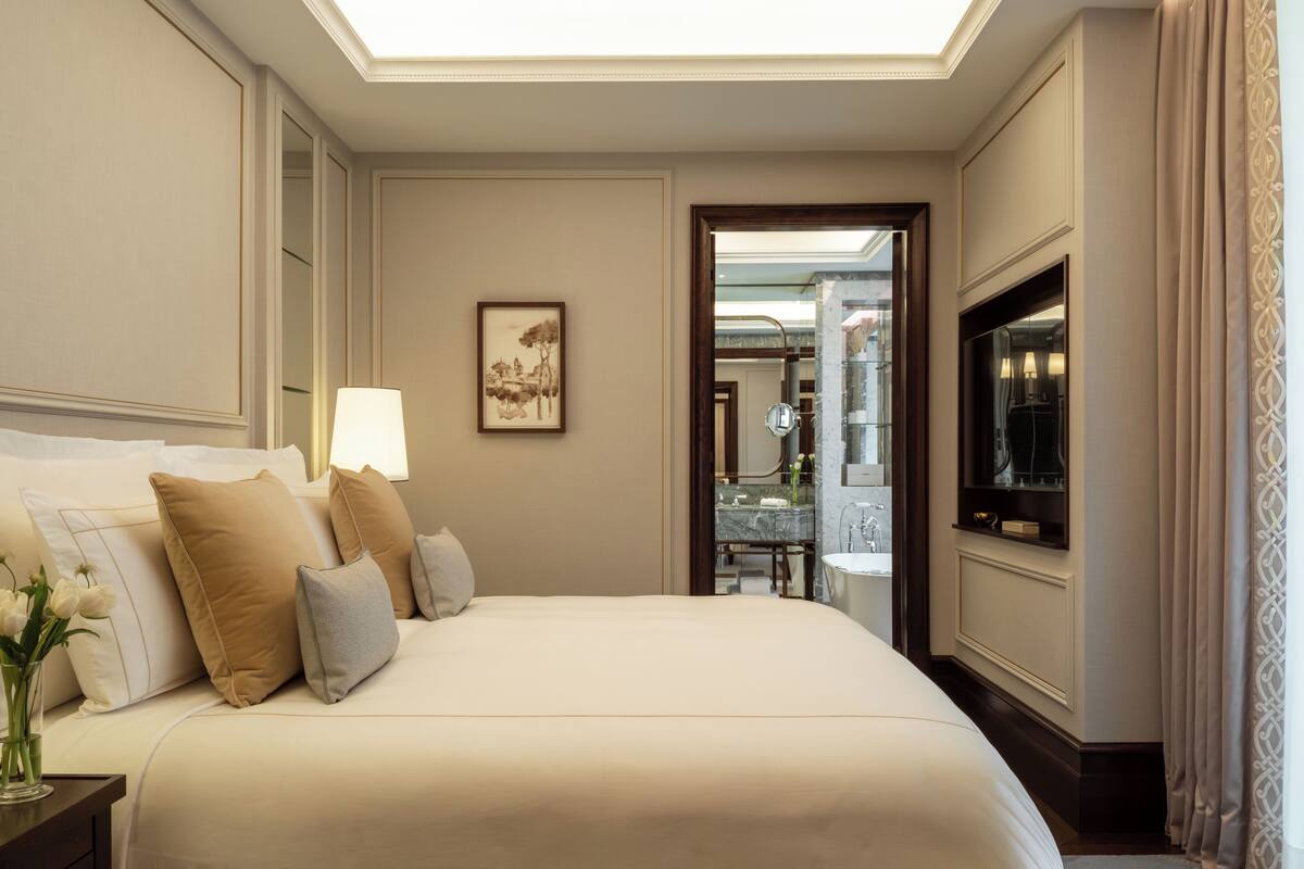 A hotel room with a large bed, a bedside table with a lamp, a framed picture on the wall, and a bathroom visible through an open door.