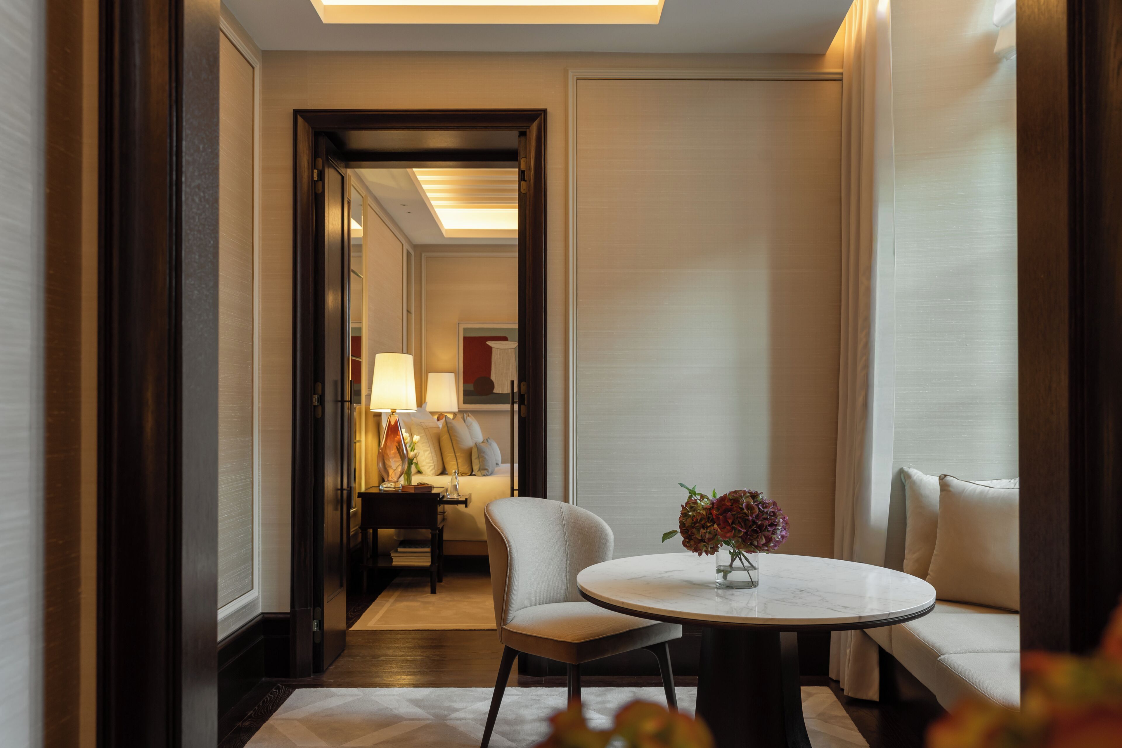 A hotel room with a round table, a sofa, a lamp, and a bed in the background.