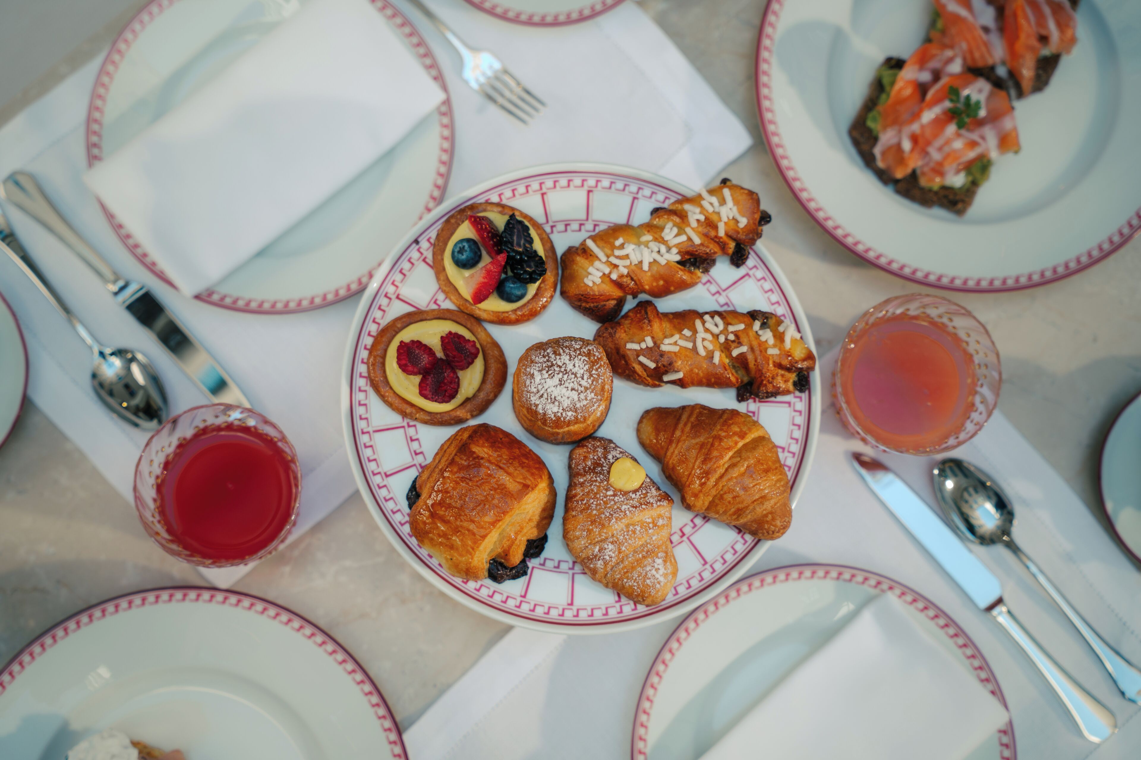A table set with plates of pastries, a glass of red drink, and silverware.