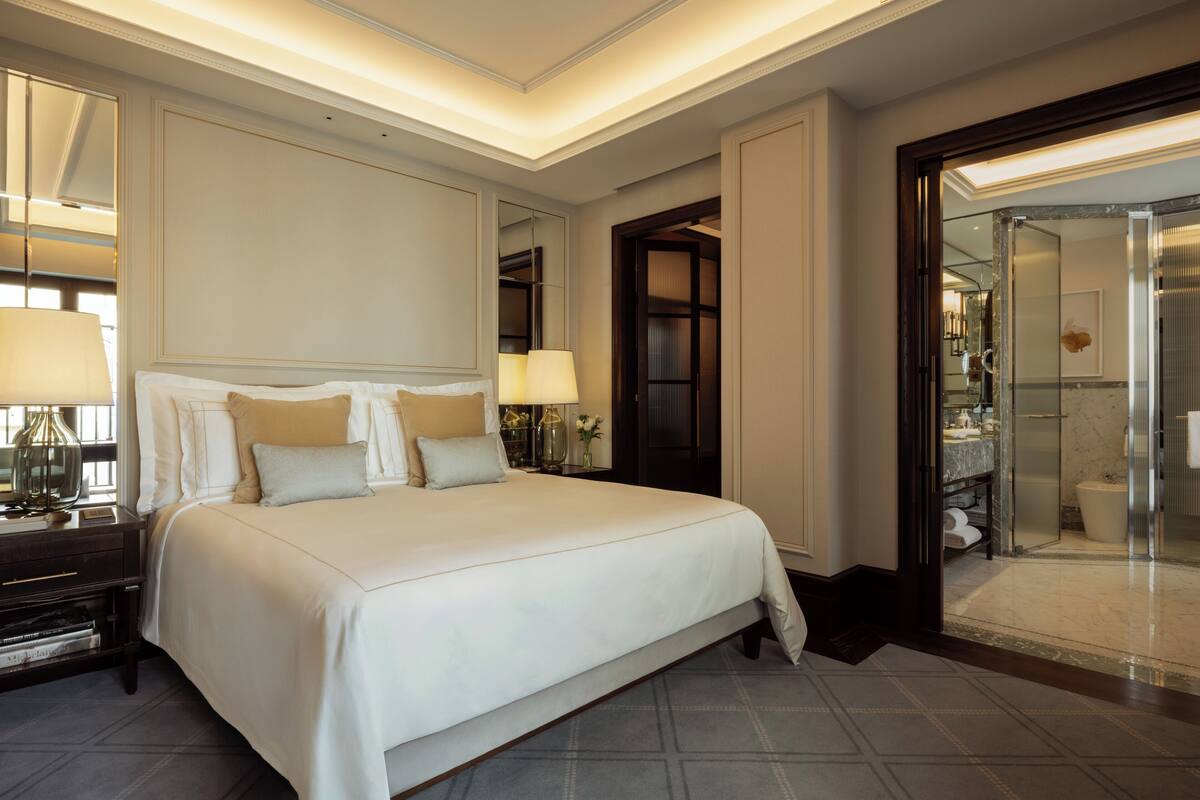 A hotel room with a large bed, bedside lamps, a nightstand, and a bathroom with a glass shower enclosure.