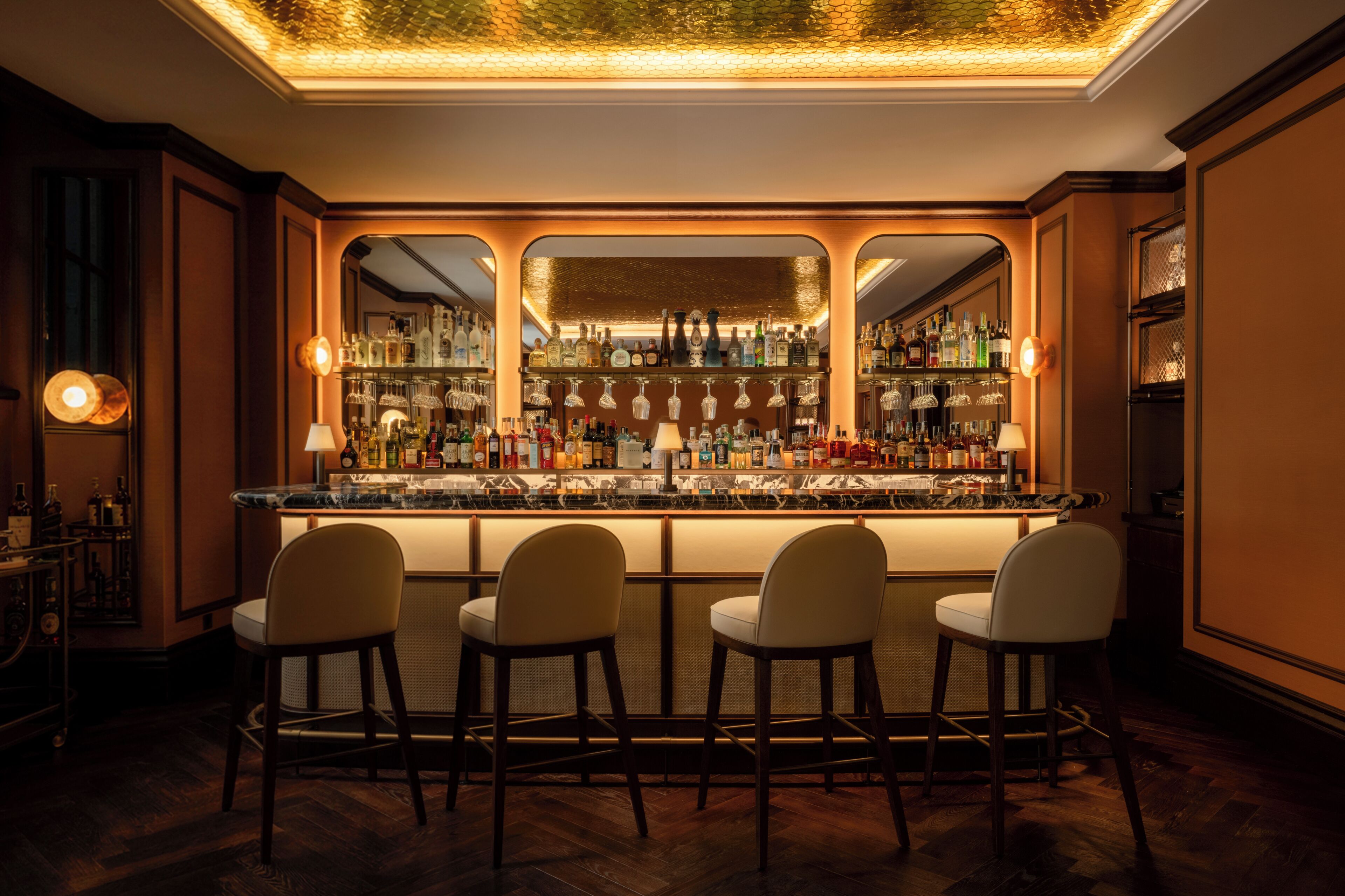 Un espace bar doté d’un comptoir en marbre, de nombreuses bouteilles d’alcool et de tabourets de bar.