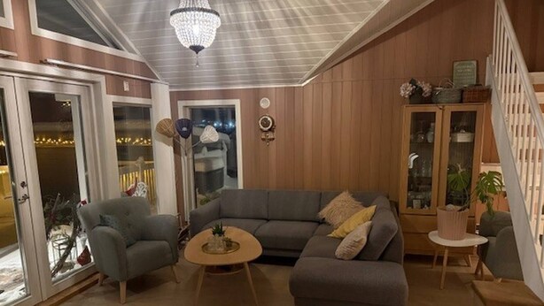 A cozy living room with a grey sectional sofa, a small round coffee table, and a chandelier. - Cottage for Rent by the sea (Narvik)