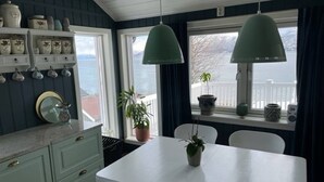 A kitchen with a white table, two pendant lights, a potted plant, and a window with a view of the sea. - Cottage for Rent by the sea (Narvik)