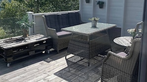 An outdoor patio with wicker furniture, a wooden deck, and a view of mountains and trees. - Cottage for Rent by the sea (Narvik)