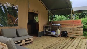 Un espacio al aire libre con carpas, un sofá, una mesa con utensilios de cocina y vistas a zonas verdes.