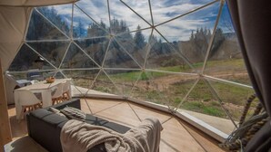 A geodesic dome interior with a dining area, sofa, and a view of a forested landscape. - ZEcamping 3* piscine couverte dog friendly locatif BBQ clim 50m2 (Châtel-Montagne)