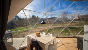 A tent with a wooden table and chairs, a hanging light, and a view of a hilly landscape. - ZEcamping 3* piscine couverte dog friendly locatif BBQ clim 50m2 (Châtel-Montagne)
