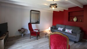 Un salon avec un canapé gris, un fauteuil rouge, une télévision et un miroir au mur.