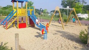 A playground with a slide, swings, and a climbing structure. - ZEcamping 4* familial piscine couverte jacuzzi sauna locatif TV 24m2 (Caro)