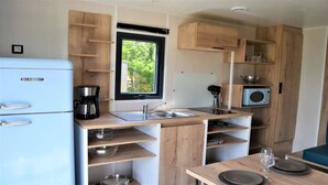 A compact kitchen with a blue refrigerator, wooden cabinets, a window, and a microwave. - ZEcamping 4* familial piscine couverte jacuzzi sauna locatif TV 24m2 (Caro)