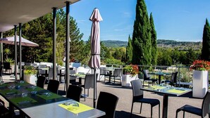 Une terrasse extérieure avec des tables et des chaises, entourée de verdure et d’arbres, et offrant une vue sur le paysage.