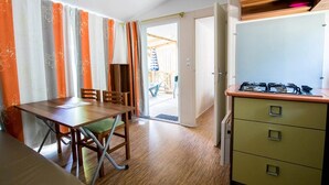 Une cuisine compacte équipée d’une cuisinière à gaz, d’une table à manger avec des chaises et d’une porte coulissante donnant sur un espace extérieur.