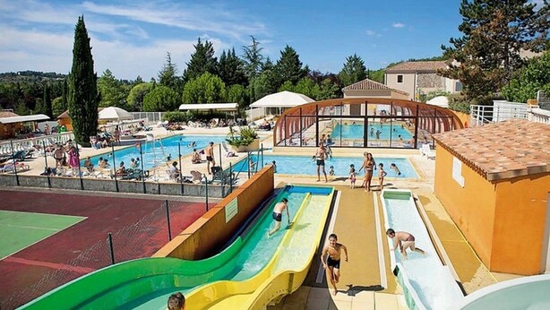 Un espace piscine comprenant plusieurs bassins et toboggans, entouré d’arbres et de bâtiments.