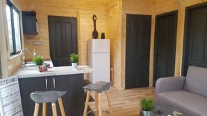 A compact kitchen with a white countertop, two stools, a refrigerator, and a sign indicating a dining area. - ZEcamping 4* animé piscine couverte locatif TV LV (Caro)