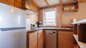 Une cuisine compacte dotée de meubles en bois, d’un lave-vaisselle, d’une machine à café et d’une fenêtre laissant entrer la lumière naturelle.