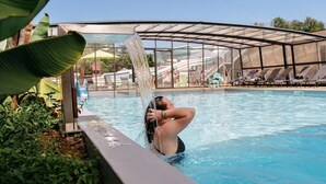 Une piscine dotée d’un espace clos par des parois de verre, entourée de chaises longues et de verdure.