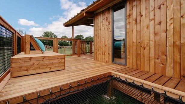 Une terrasse en bois avec un toboggan et une zone de piscine protégée par un filet.