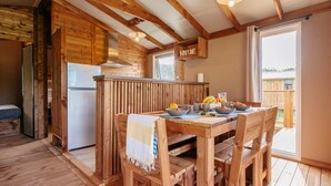 Une cabane en bois avec un coin cuisine comprenant une table à manger dressée pour le petit-déjeuner, un réfrigérateur et un panneau indiquant « NATURE ».