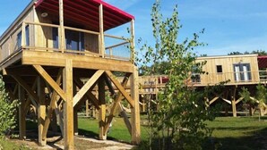 A wooden structure with a red roof, elevated on stilts, surrounded by greenery.
