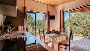 A modern kitchen with a large window, a dining area with a table set for two, and a view of trees outside.