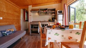 A cozy cabin interior with a dining table set for breakfast, a sofa, and a kitchen area with shelves and appliances.