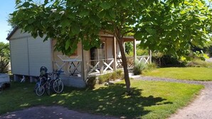 Une petite maison avec un porche, un vélo garé devant et un arbre à l’avant.