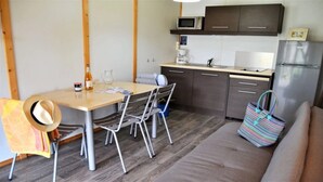Une cuisine compacte équipée d’un four à micro-ondes, d’une machine à café et d’un réfrigérateur. On y trouve une table à manger avec des chaises, ainsi qu’un canapé dans l’espace salon.