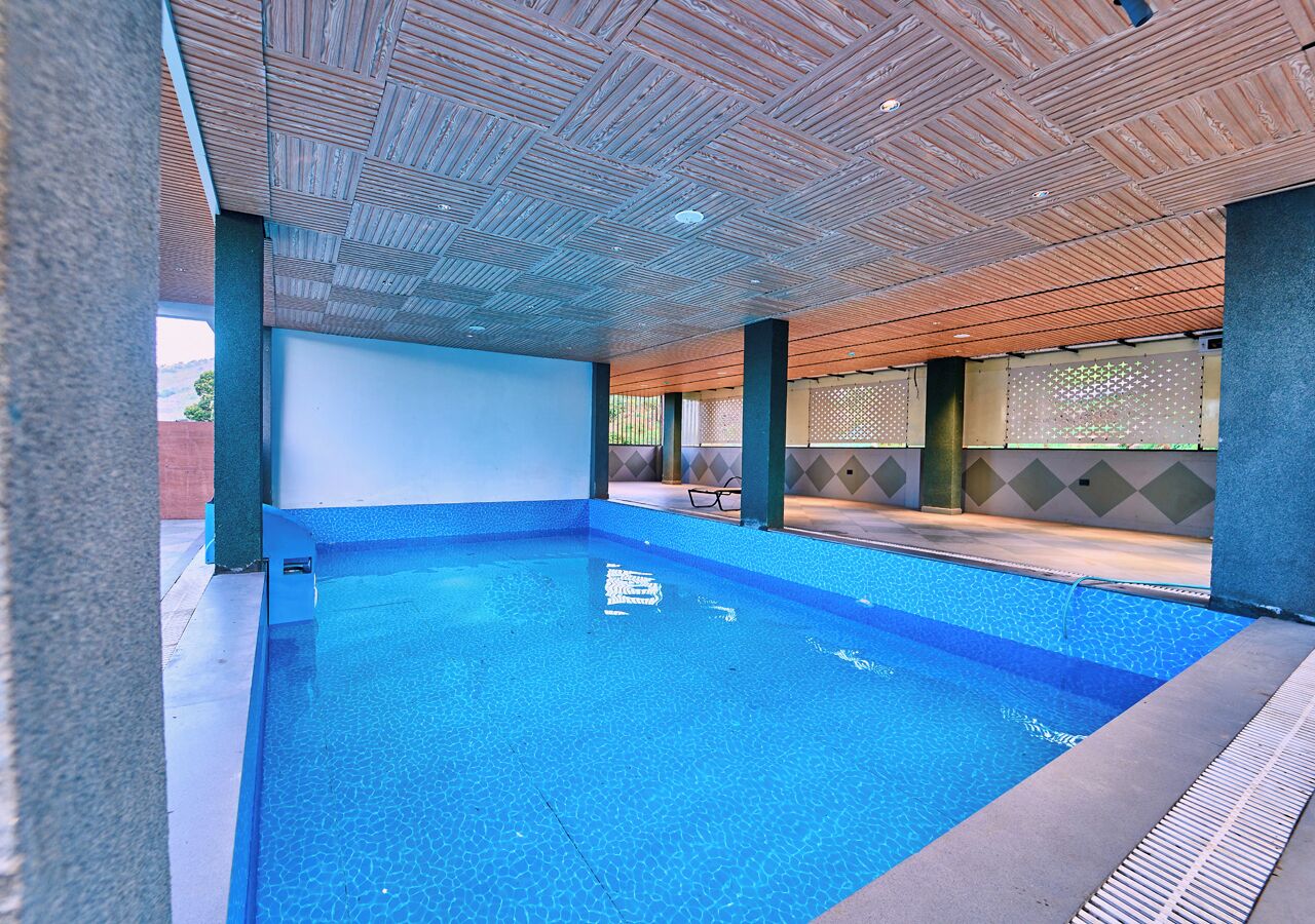 Una piscina interior con agua azul cristalina, rodeada de un suelo de baldosas y un techo de madera.