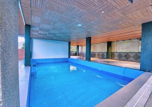 An indoor swimming pool with clear blue water, surrounded by a tiled floor and a wooden ceiling. - Cloudskape Resort Ooty by VOYE HOMES (Ooty)
