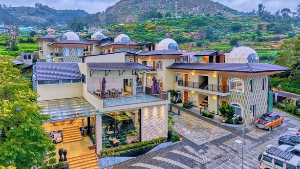 A modern hotel with multiple dome-roofed buildings, a central courtyard, and a mountainous backdrop. - Cloudskape Resort Ooty by VOYE HOMES (Ooty)