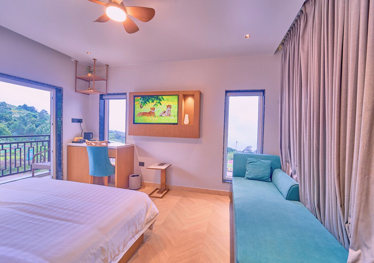 Habitación de hotel con cama, escritorio, silla, mesita, un cuadro y vistas al exterior.