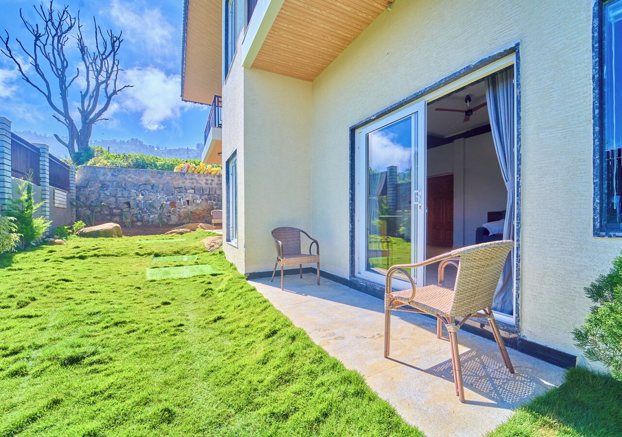A modern house with a patio, two wicker chairs, and a stone wall.
