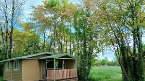 Une petite cabane à un seul étage, dotée d’un porche et entourée d’arbres et d’herbe.