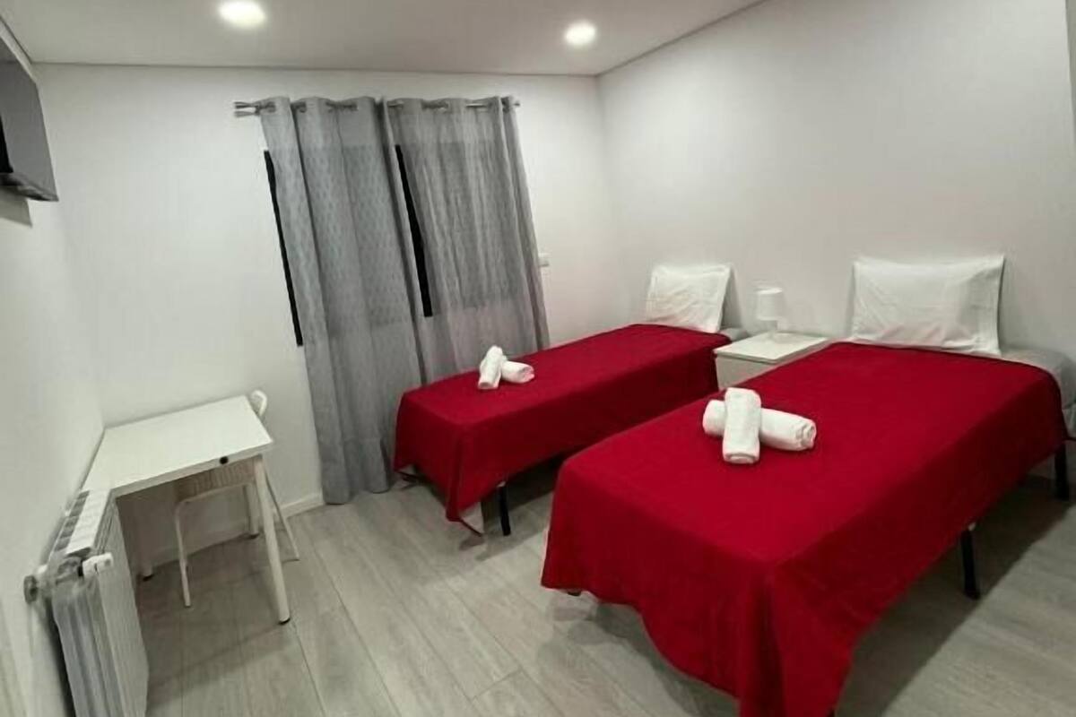 A hotel room with two single beds, a small desk, and a TV.