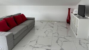 A modern living room with a grey sofa, red cushions, a white cabinet, and a TV on a white stand. - In Barcelos View Lodge (Barcelos)