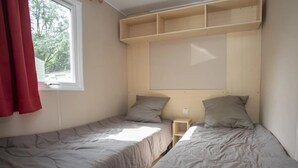 Ein Schlafsaalzimmer mit zwei Einzelbetten, einem Fenster mit roten Vorhängen und einem Holzboden darüber.