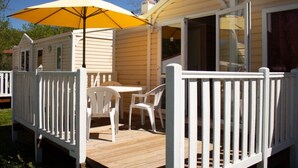 Ein Mobilheim mit Terrasse, Tisch, zwei Stühlen und einem gelben Sonnenschirm.
