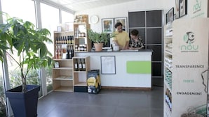 A reception area with a counter, shelves with bottles, a potted plant, and a large window. - ZEcamping 4* pataugeoire animaux acceptés cottage TV LV clim 32m2 (Foix)